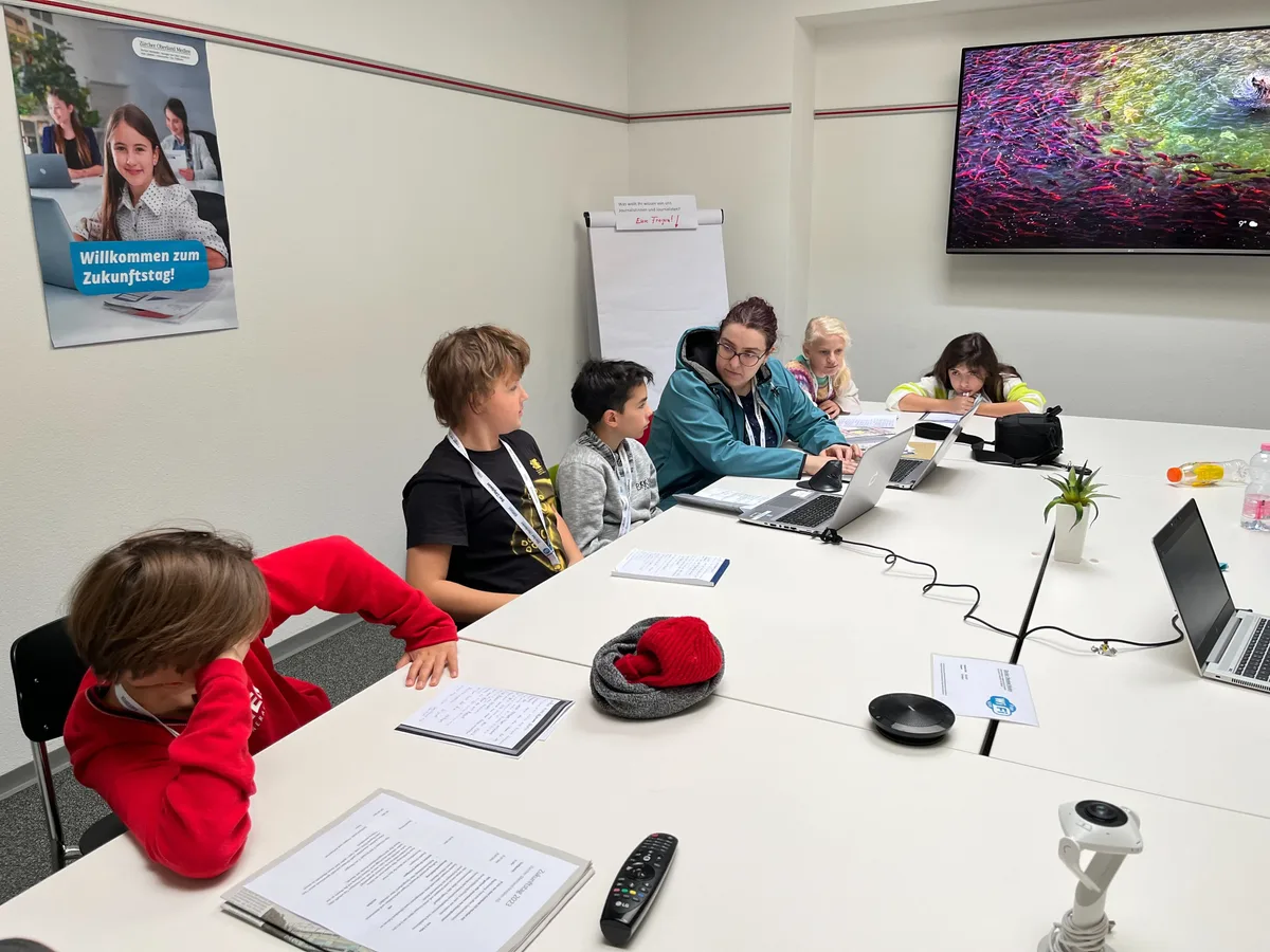 Zurück auf der Redaktion steht die Schreibarbeit an. Eine Redaktorin sitzt mit Kindern in einem Sitzungszimmer.