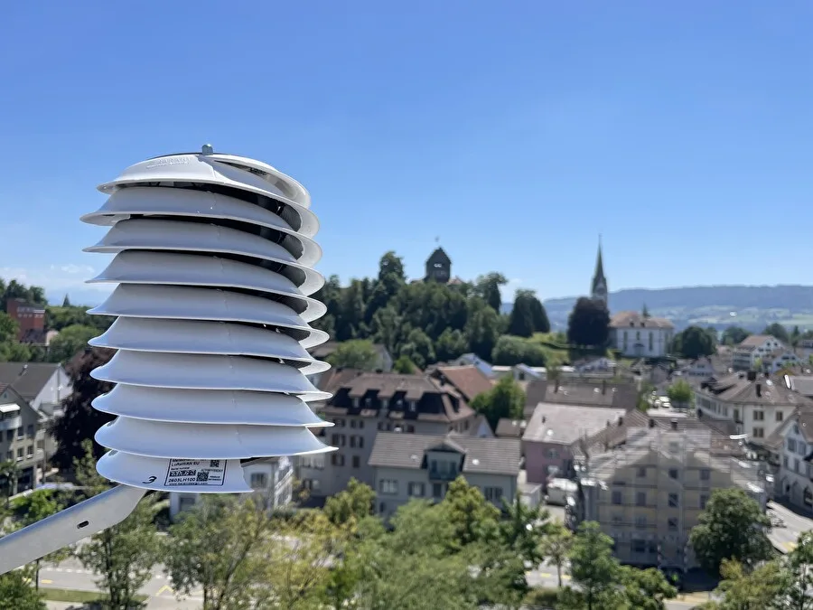 noneDie zwölf Sensoren wurden an verschiedenen, bewusst gewählten Orten in Uster installiert. Man sieht ein weisses Gerät vor der Kulisse der Stadt Uster.