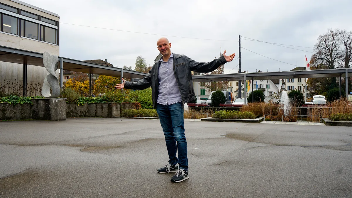 Man sieht einen Mann auf einem Platz, der die Arme ausstreckt. 