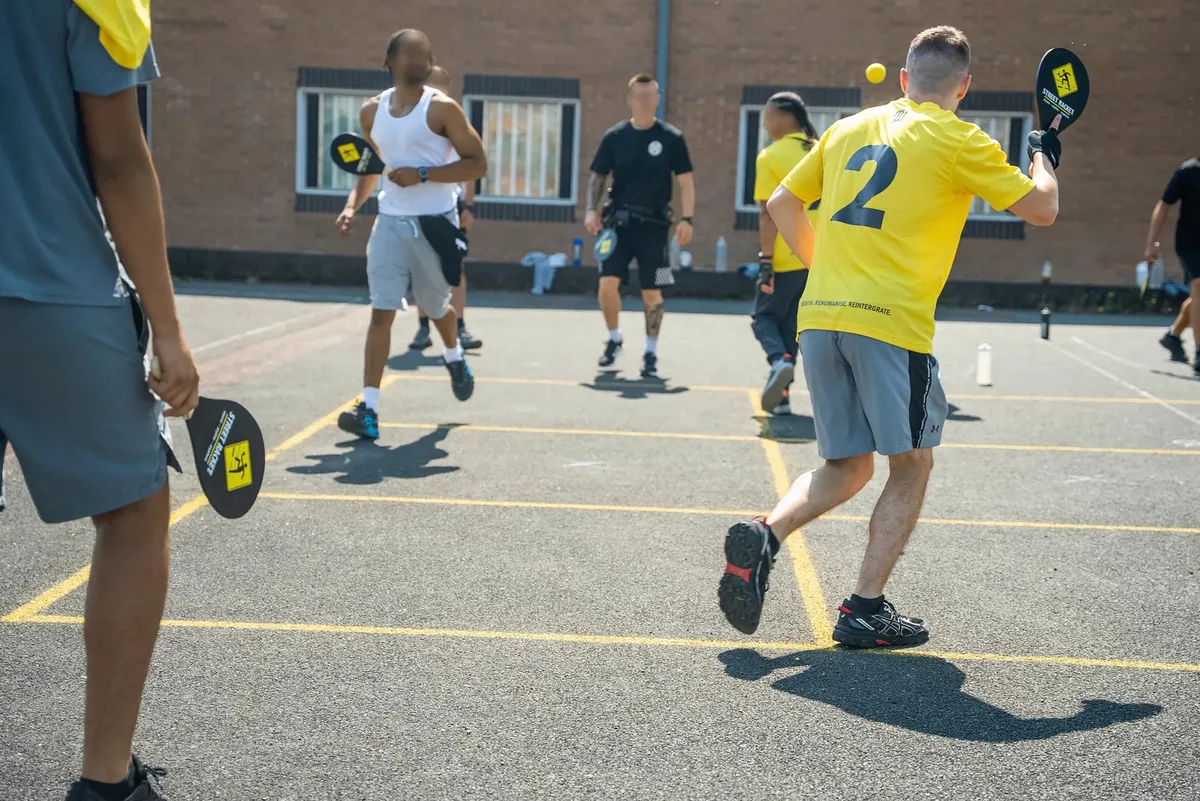 Man sieht eine Gruppe von Häftlingen Street Racket spielen.