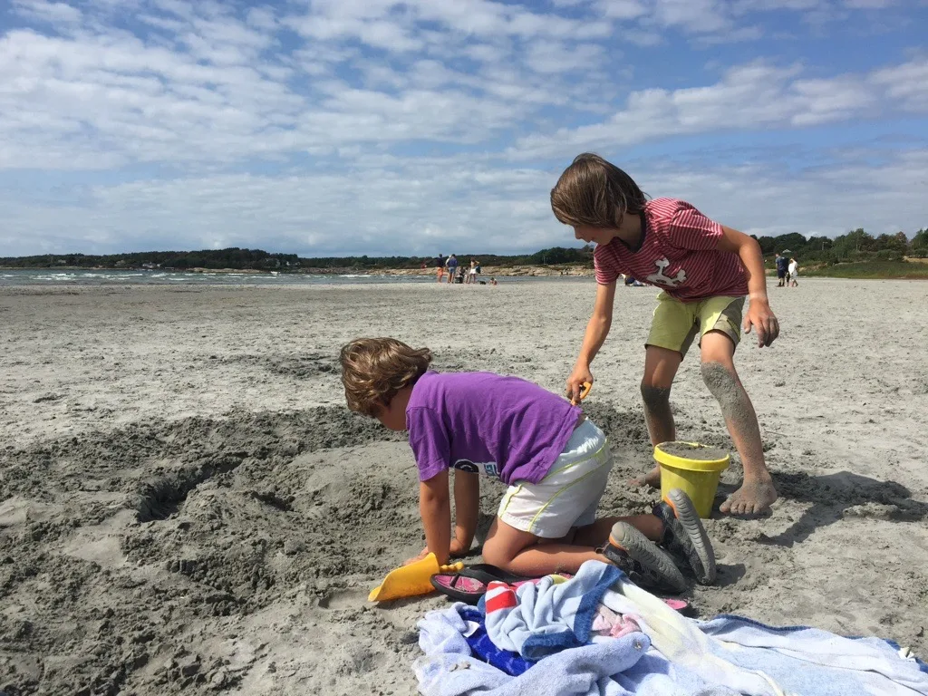 Man sieht zwei Kinder am Sandstrand spielen.