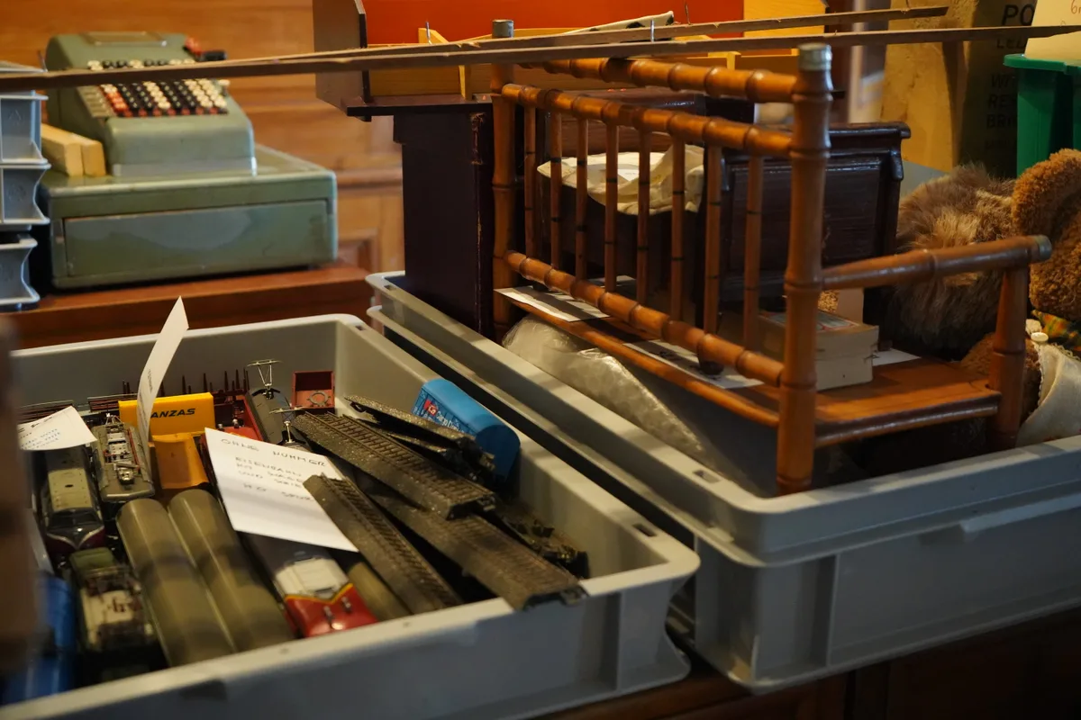 Spielzeuge in Kisten, dahinter eine alte Kasse.