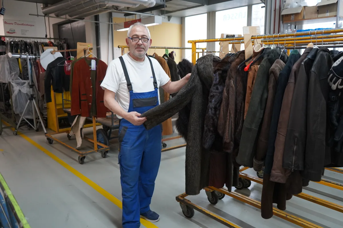 Ein Pelzfachmann steht neben einem Kleiderständer mit mehreren Pelzen.