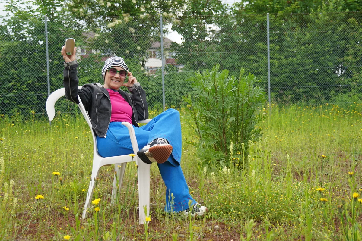 Lilian Frei sitzt auf einem kaputten Plastikstuhl auf dem verwilderten Tennisplatz.