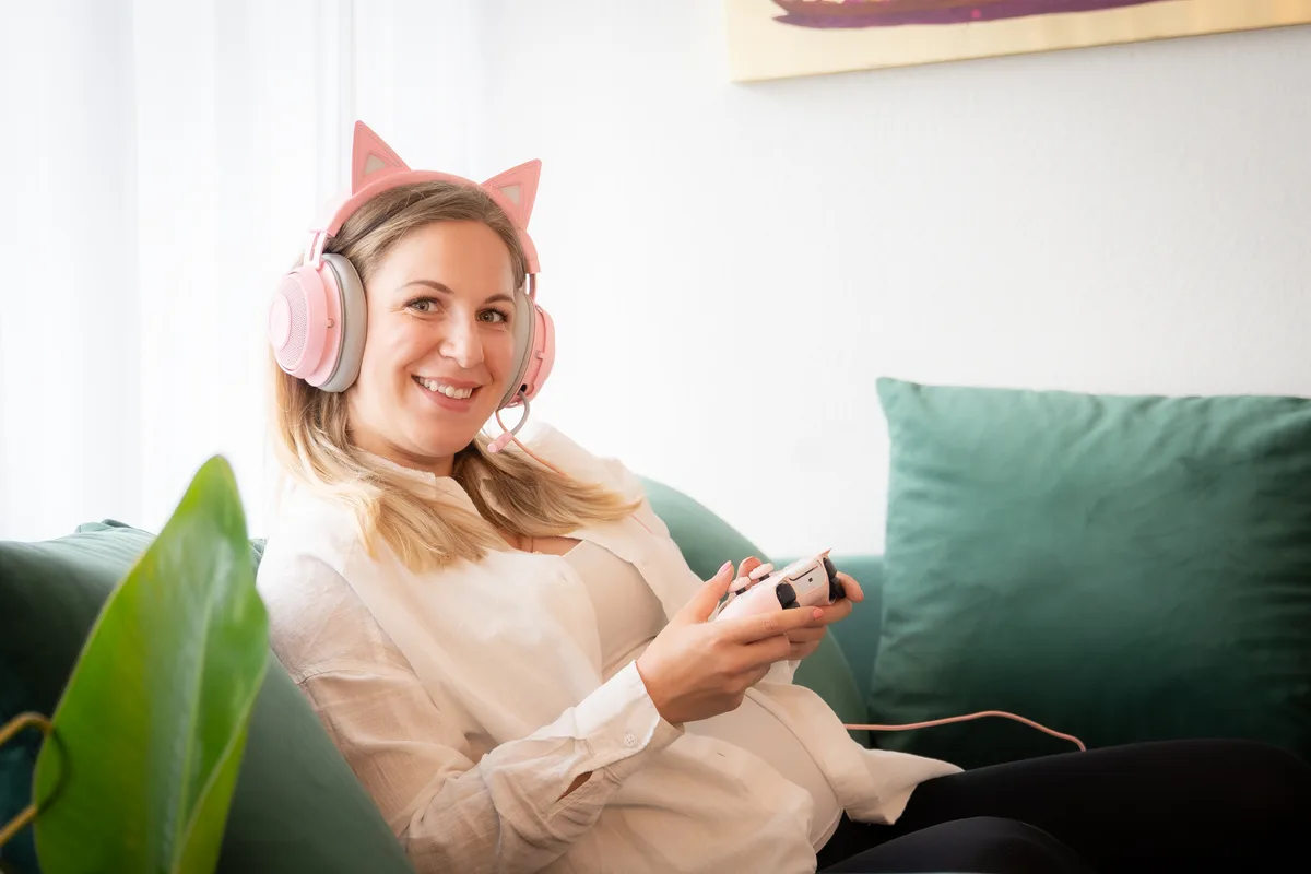 Eine Frau hält auf dem Sofa einen Controller in der Hand. 