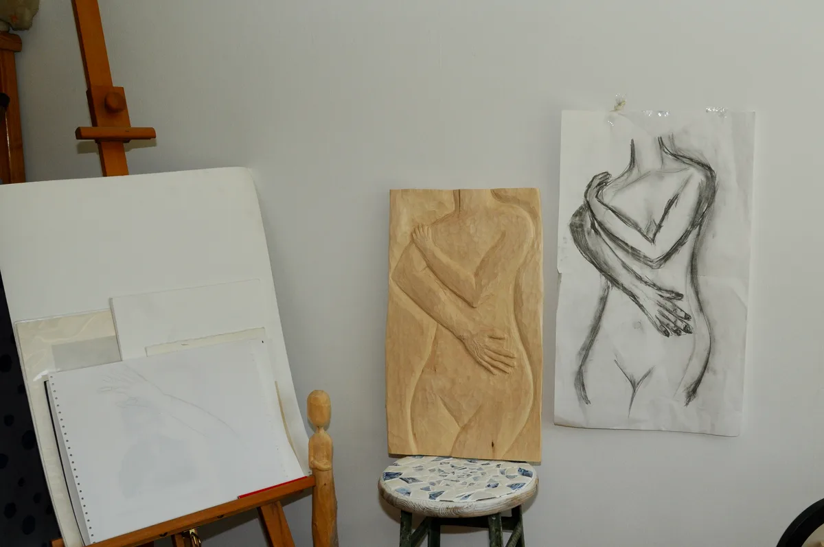 Man sieht eine Leinwand, Skizzen und ein Holzrelief.