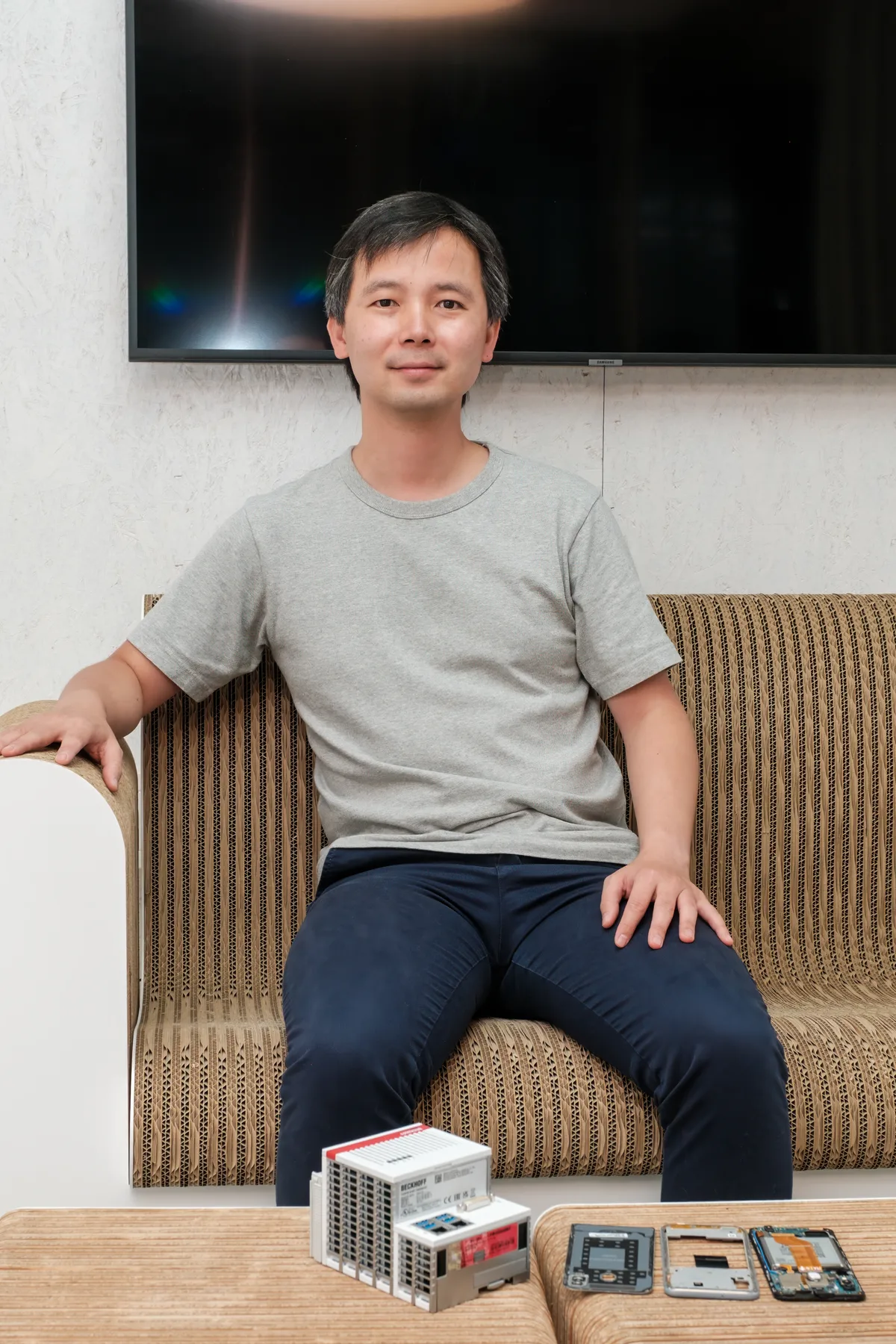 Ein Mann sitzt vor einem Tisch, auf dem Smartphonkomponenten liegen.