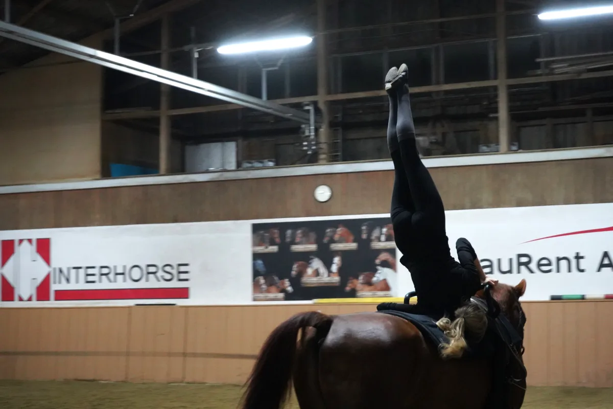 Leonie Linsbichler balanciert mit Kopf und Händen auf dem galoppierenden Pferd.
