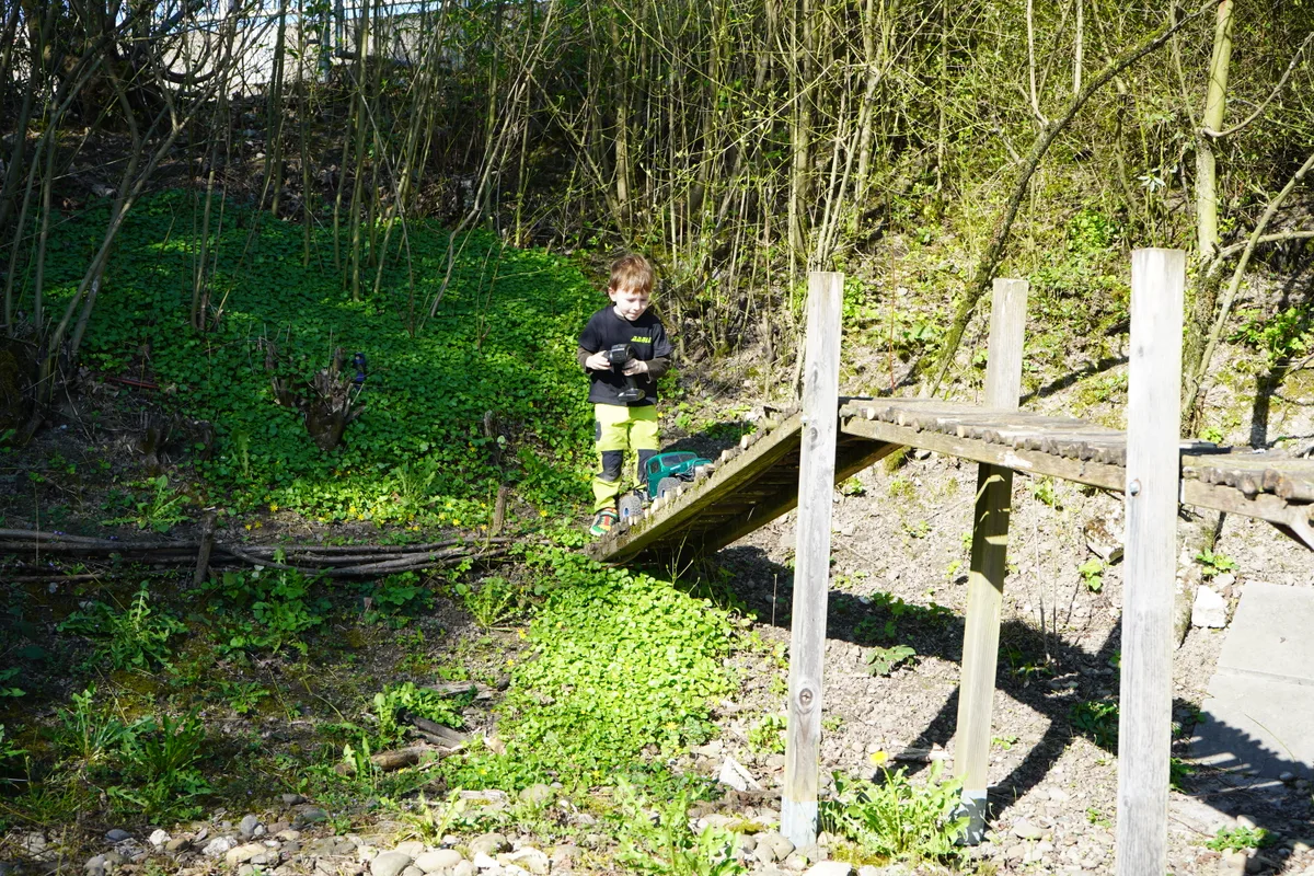 Ein Kind fährt mit einem Modellauto über eine kleine Brücke. 