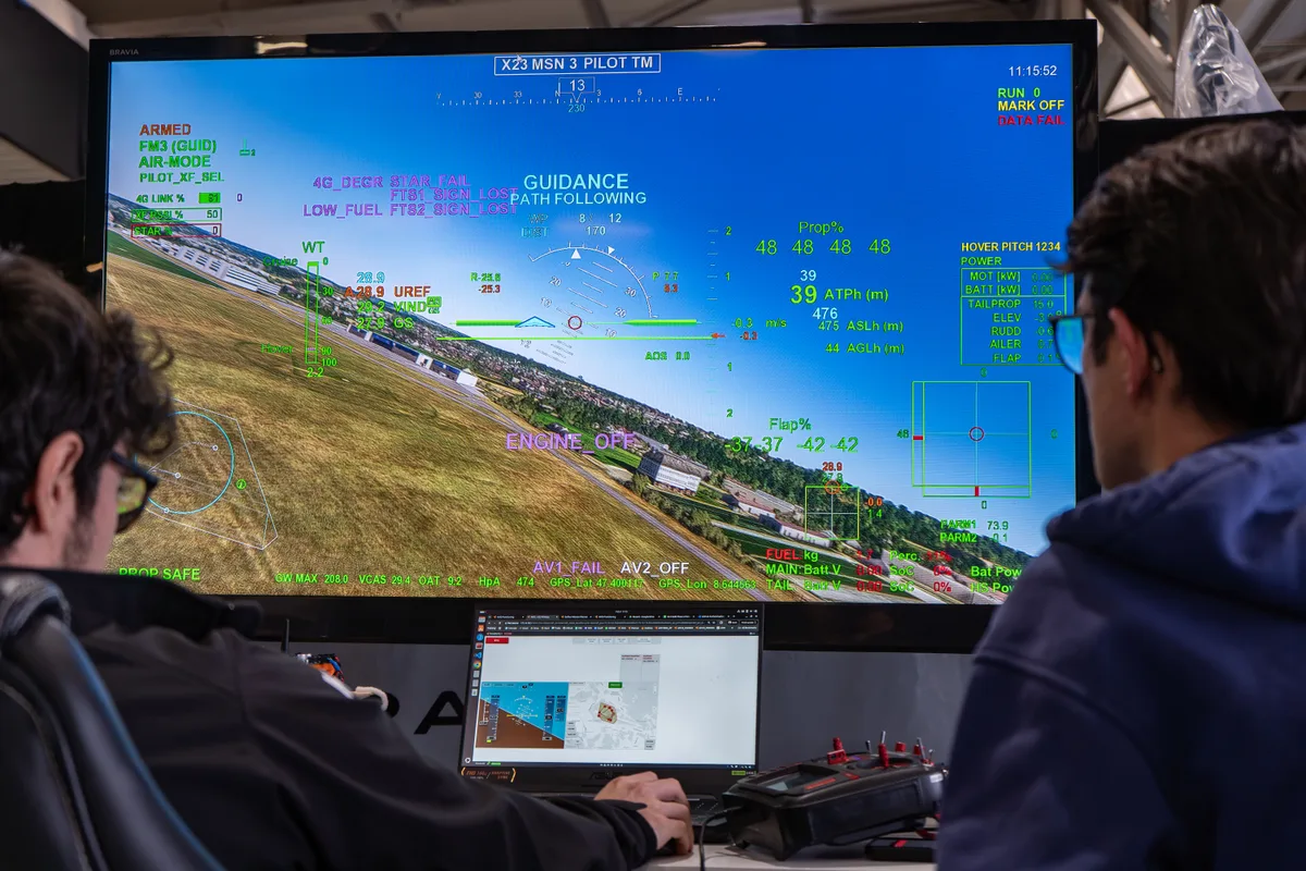 Zwei Männer sitzen vor einem Bildschirm, auf dem der Flugplatz Dübendorf abgebildet ist und auf dem der Flug der Drohne überwacht werden kann.