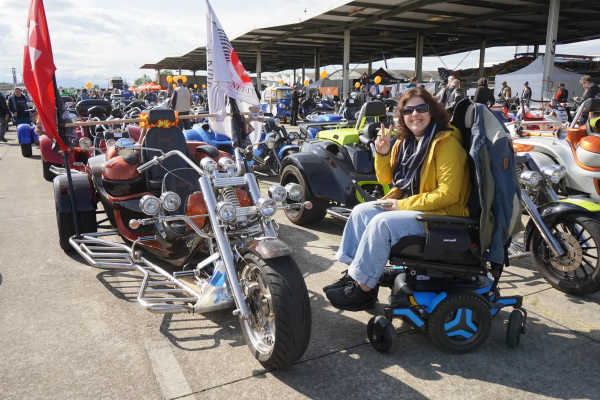 Eine Frau im Rollstuhl posiert neben einem Trike.