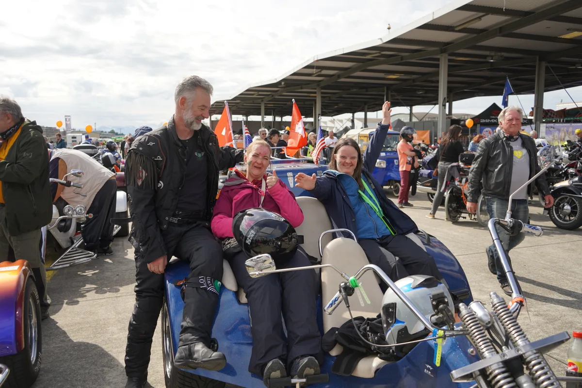 Zwei Frauen sitzen auf einem Trike, der Fahrer lehnt daran.