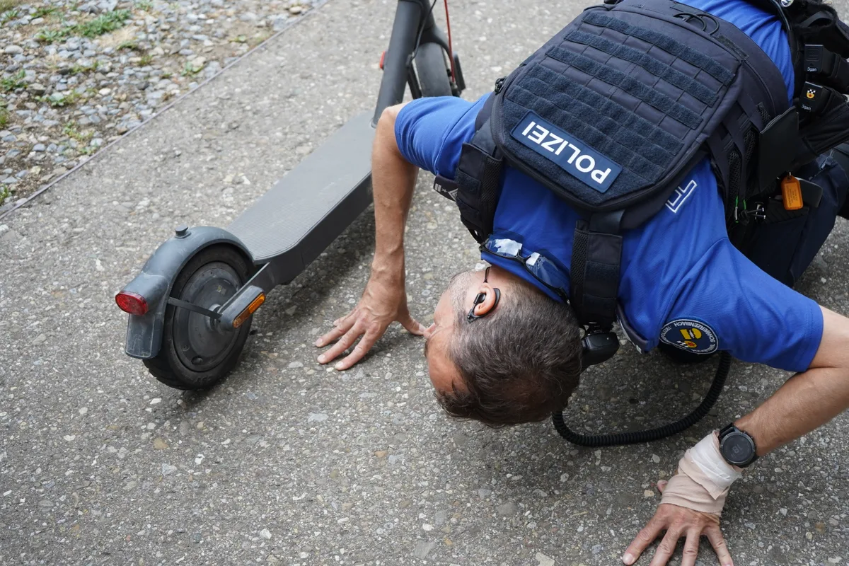 Gerber kniet auf dem Boden neben dem E-Scooter.