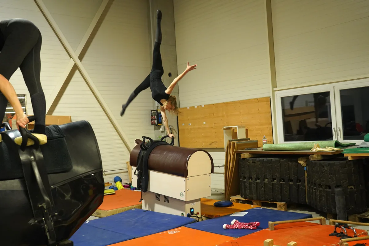 Leonie Linsbichler macht einen einarmigen Handstand mit dem Spagat auf einem Race-Wood.