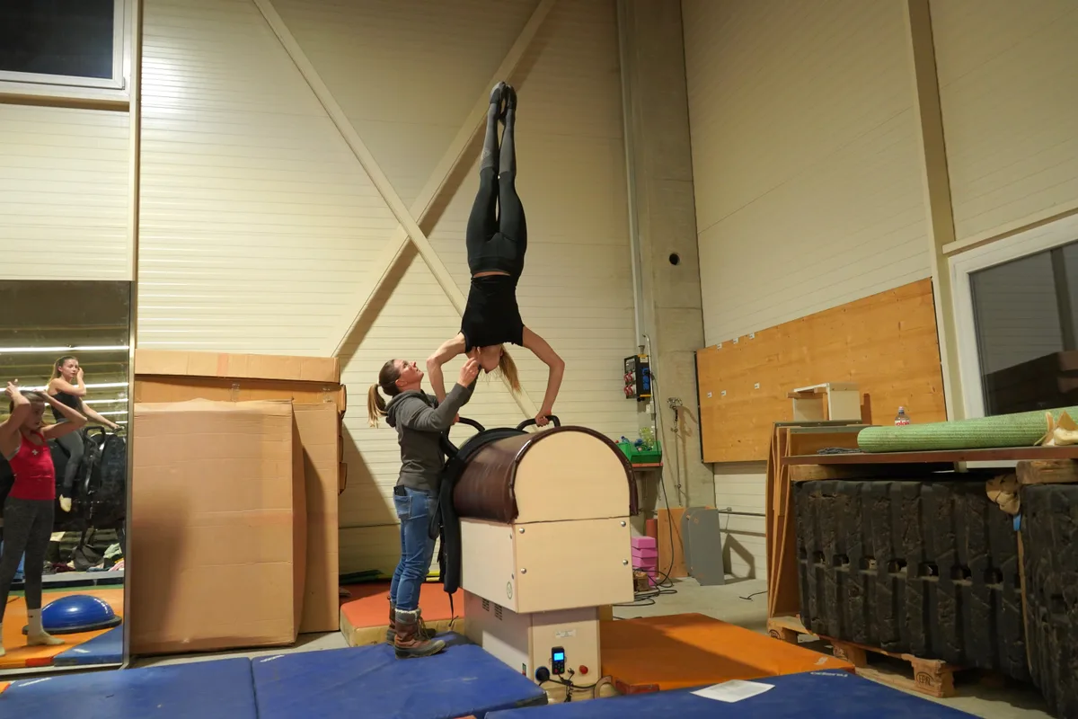 Leonie Linsbichler macht auf einem Racewood den Handstand, und ihre Trainerin gibt ihr Hilfestellung.