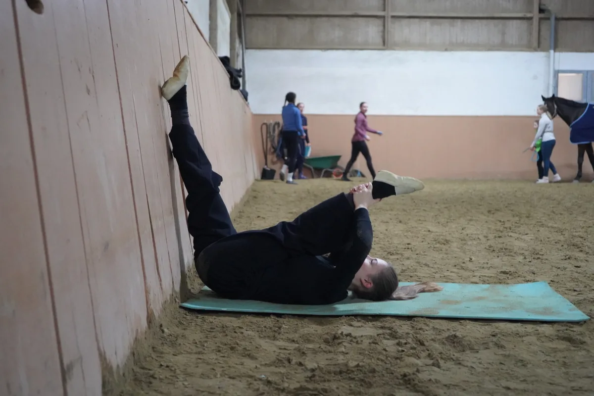 Eine Sportlerin dehnt sich auf einer Matte in einer Reithalle.