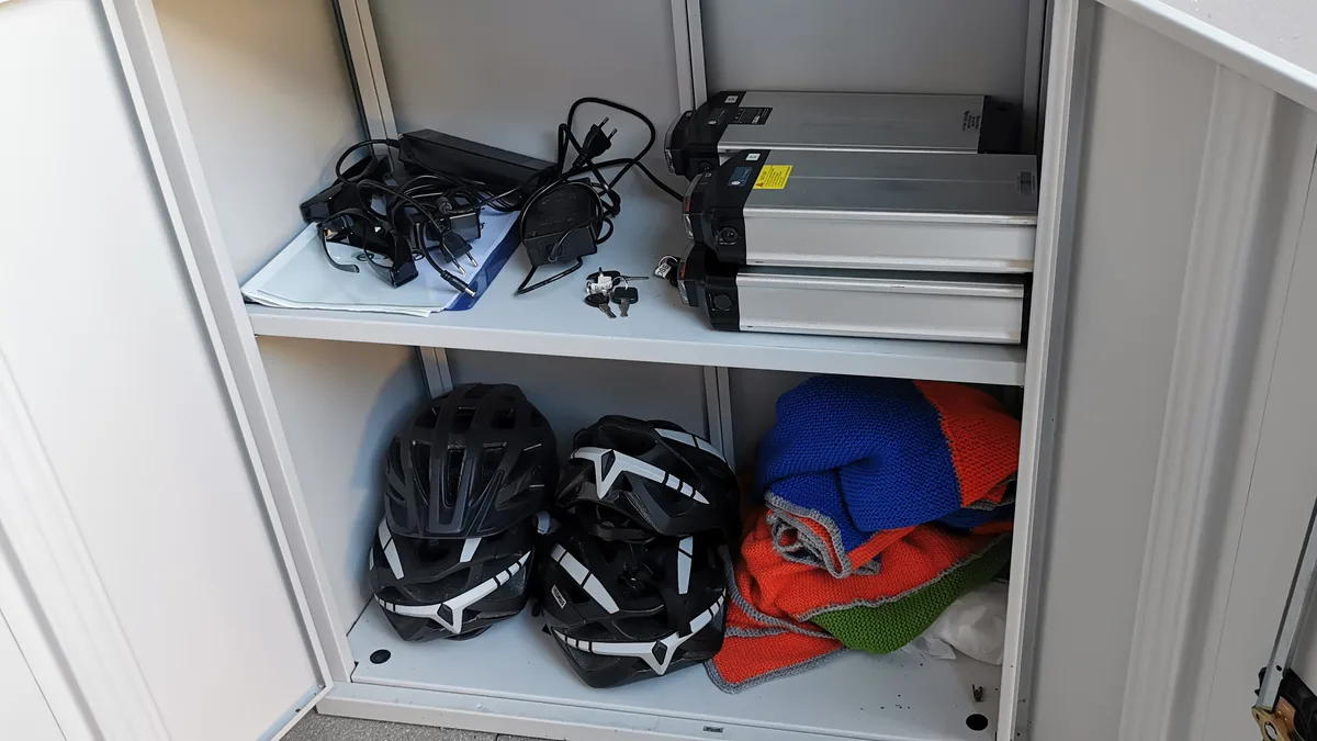Helme, Decken, E-Bike-Batterien und -Ladegeräte liegen in einem Schrank.