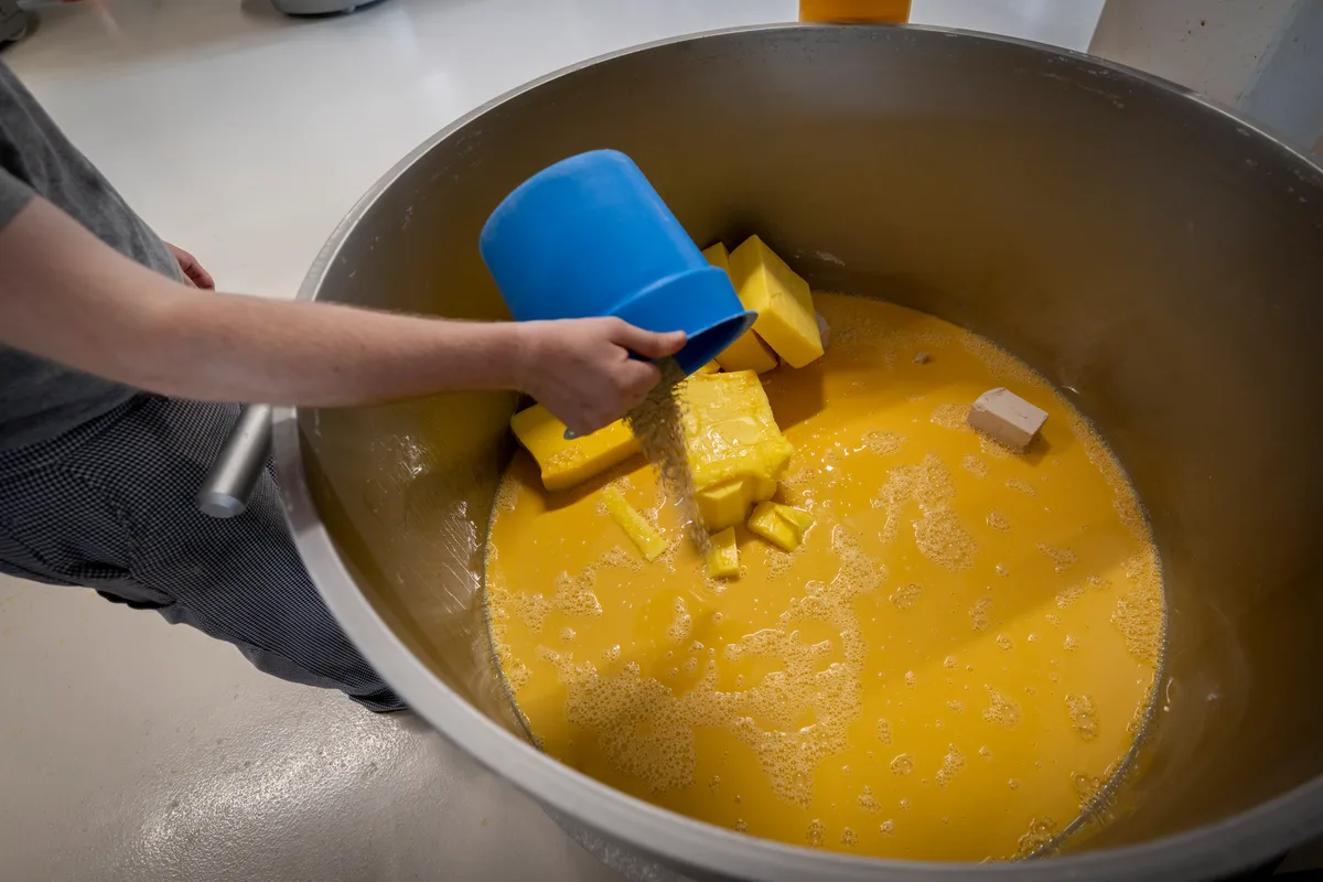 Der Teig für die Frischbackzöpfe entsteht in einem riesigen Kessel. Die Arbeiter füllen die Rohstoffe von Hand ein. Ein Arbeiter schüttet Rohstoffe in einen Kessel.