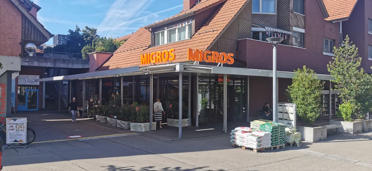 Obwohl alle drei Läden Lebensmittel verkaufen, sind die Sortimente von Migros und Coop nicht sehr ähnlich wie das des Ada Market. Der Eingang der Migros an der Marktgasse in Dübendorf.