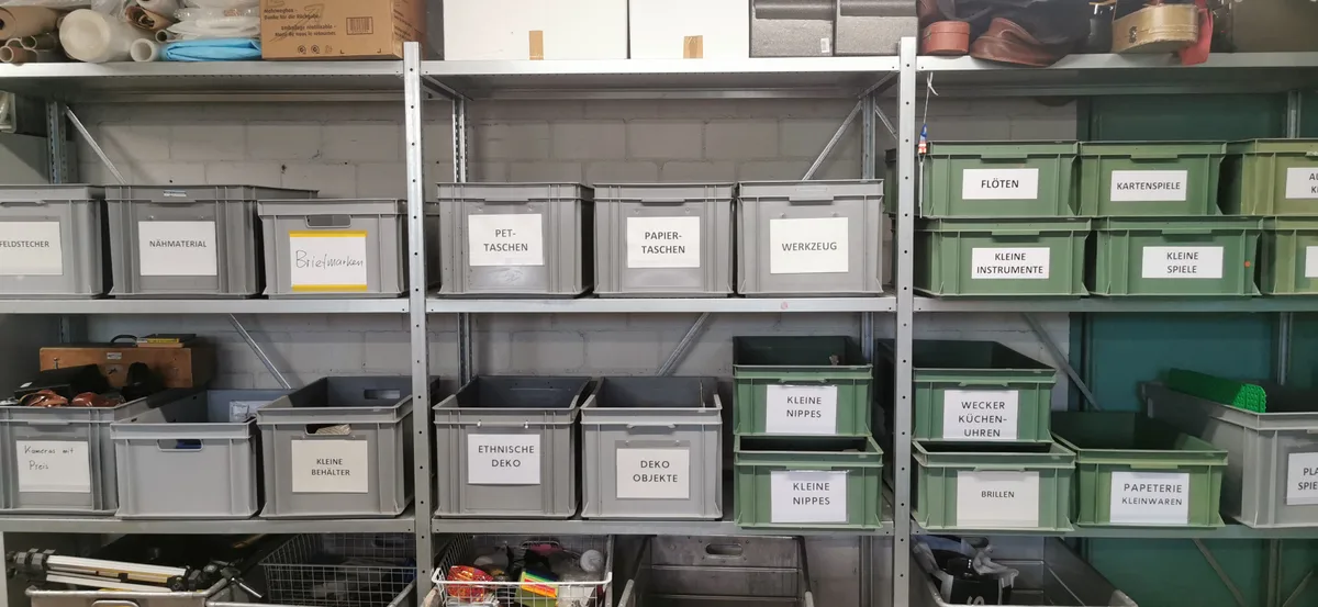 Viele Kisten, die mit Waren beschriftet sind, stehen in einem Metallregal.