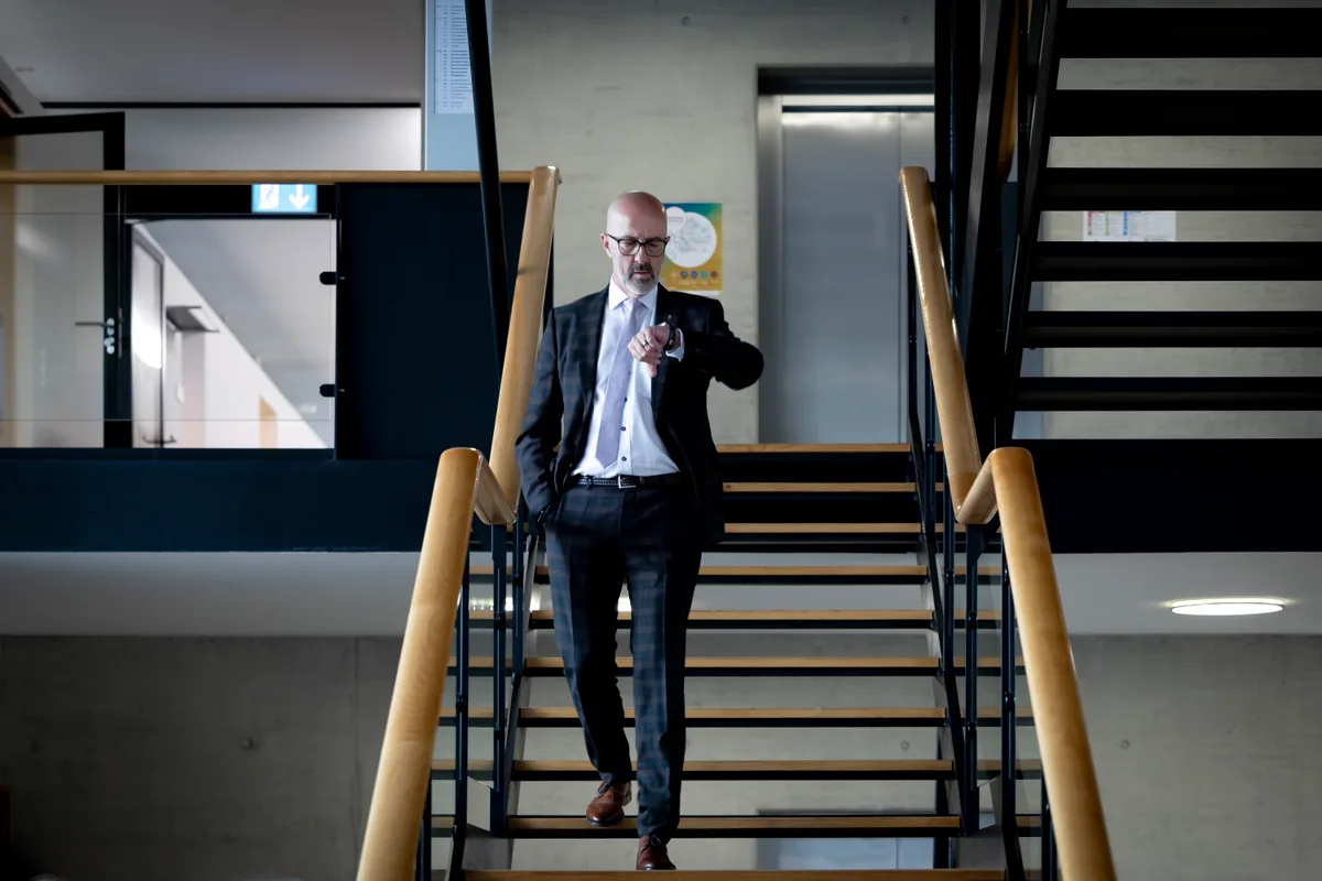 Eine Person steht auf einer Treppe und schaut auf die Uhr.