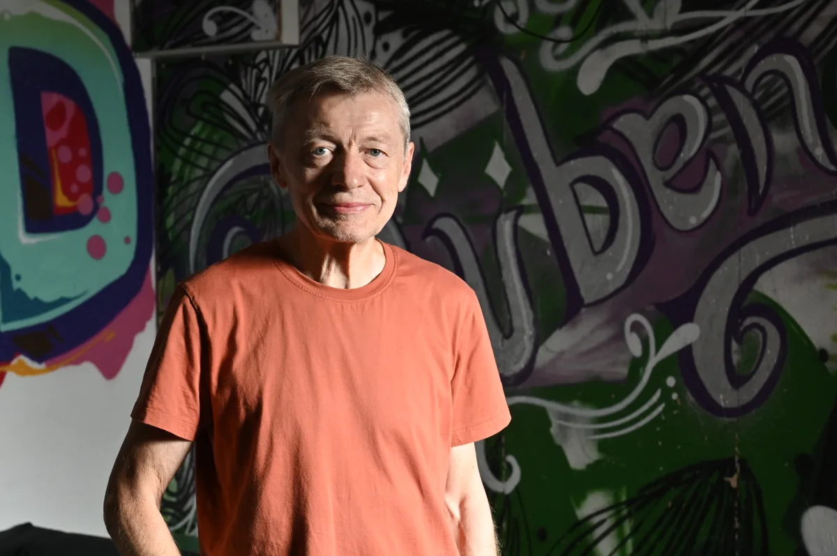 Ein Mann im T-Shirt steht vor eine Wand mit Graffiti.