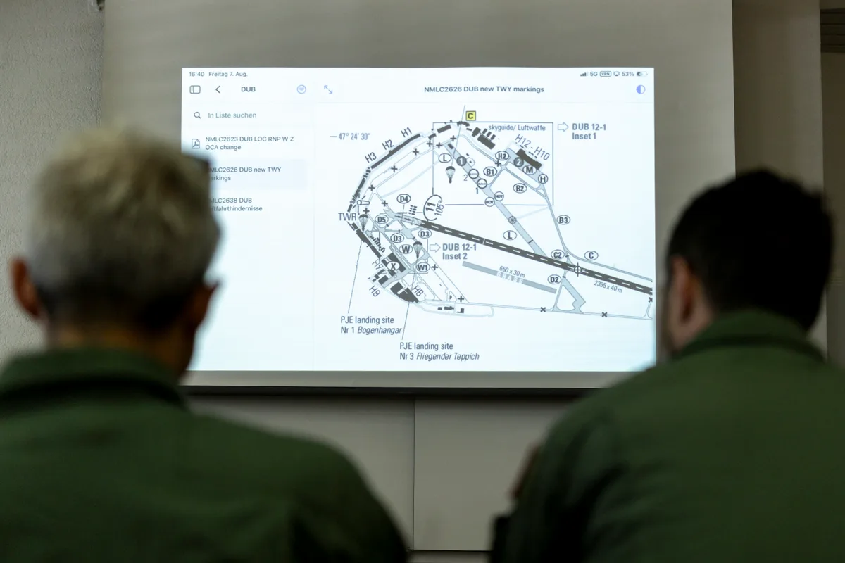 Weil sie den Dübendorfer Flugplatz noch nicht so gut kennen, machen sie sich mit der Karte vertraut. Zwei Männer schauen auf eine Leinwand.