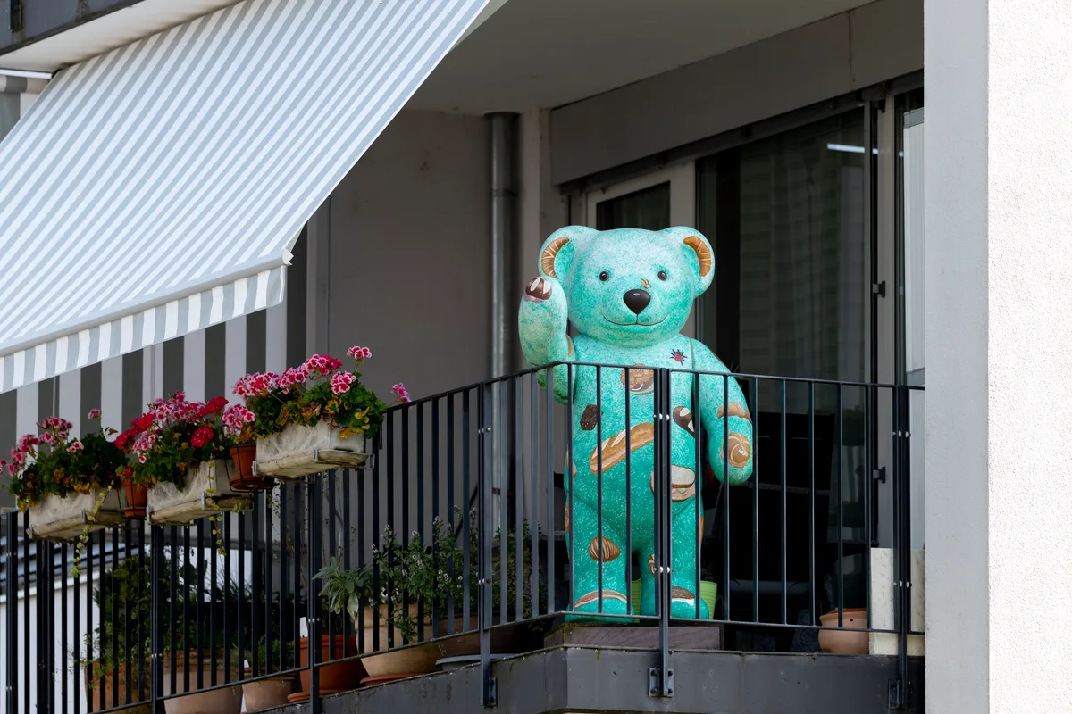 Dieser freundliche Bär winkt auf einem Balkon im Birchlen-Quartier. Ein bunt bemalter, stilisierter Teddybär auf einem Balkon.
