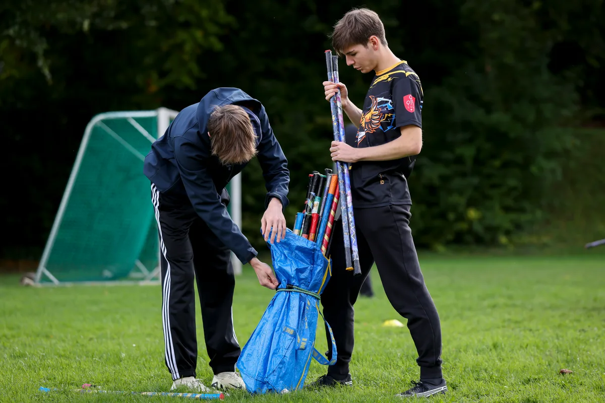 Auch einige Jugendliche, die eigentlich zu alt sind für das Kinderteam, sind auf dem Platz. Sie unterstützen Grimm beim Training. Zwei Jugendliche räumen Stöcke in einen Sack.