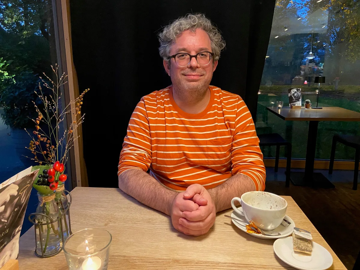 Peter Grob in farbigem Sweater an einem Tisch in einem Café.