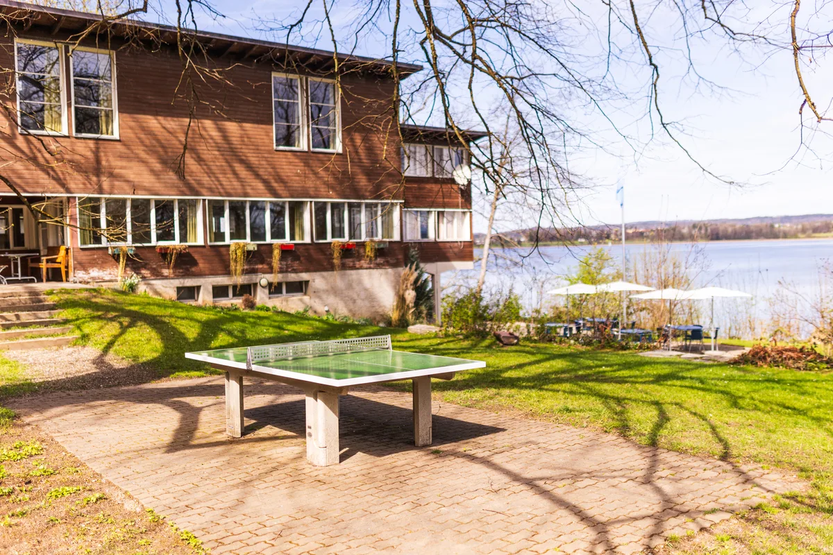 Pingpong spielen, sonnenbaden oder im Schatten sitzen: Die Jugendherberge in Fällanden ist ein guter Ort für den Sommer. Die Jugendherberge, davor ein Tischtennistisch und rechts das Greifenseeufer.