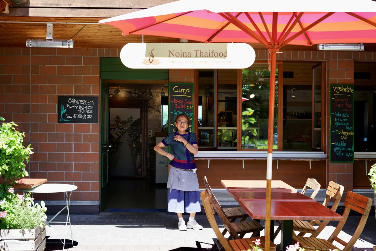 Man sieht Noina vor ihrem Restaurant stehen.