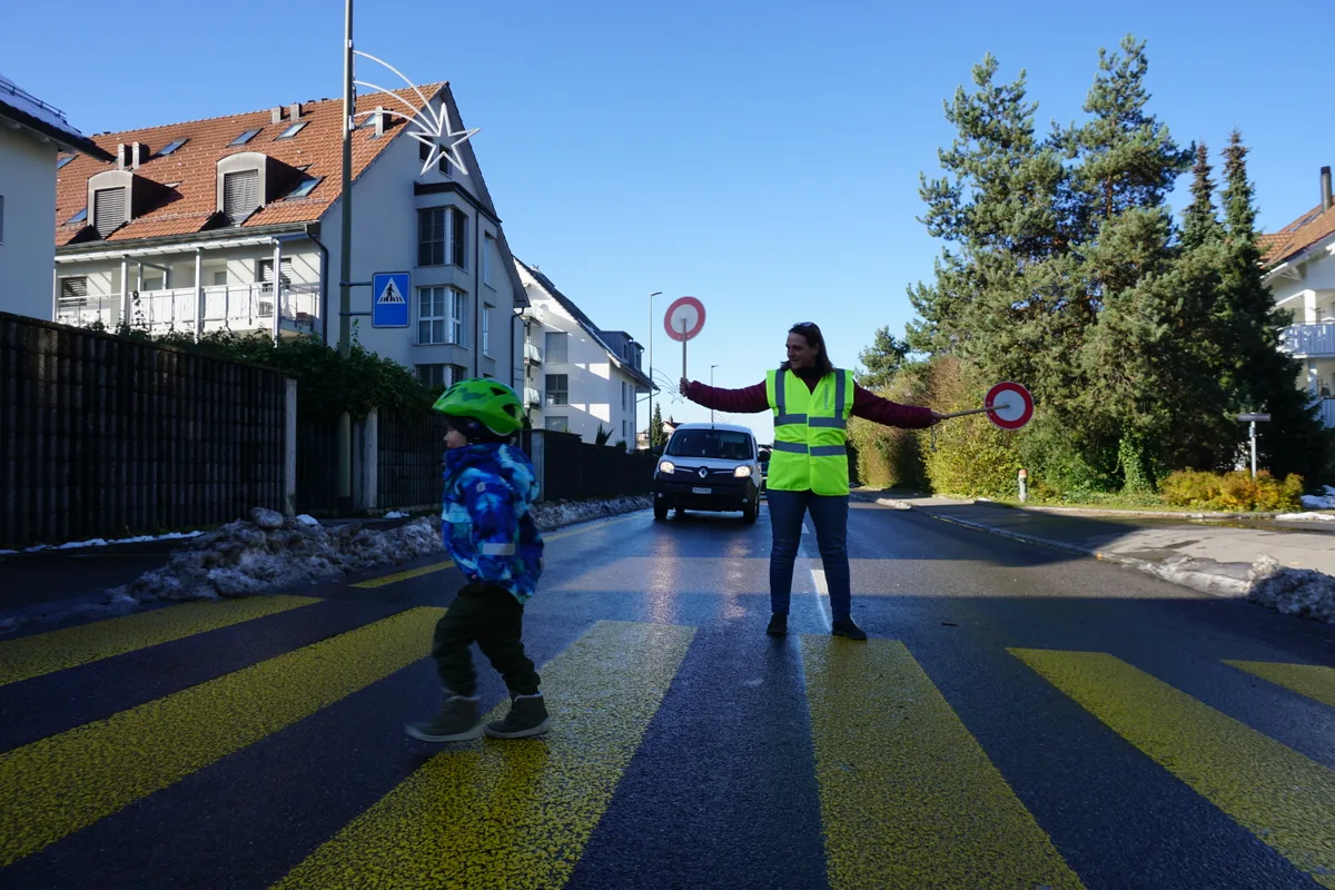 Frau hält Verkehr an und lässt Kind über Fussgängerstreifen. 