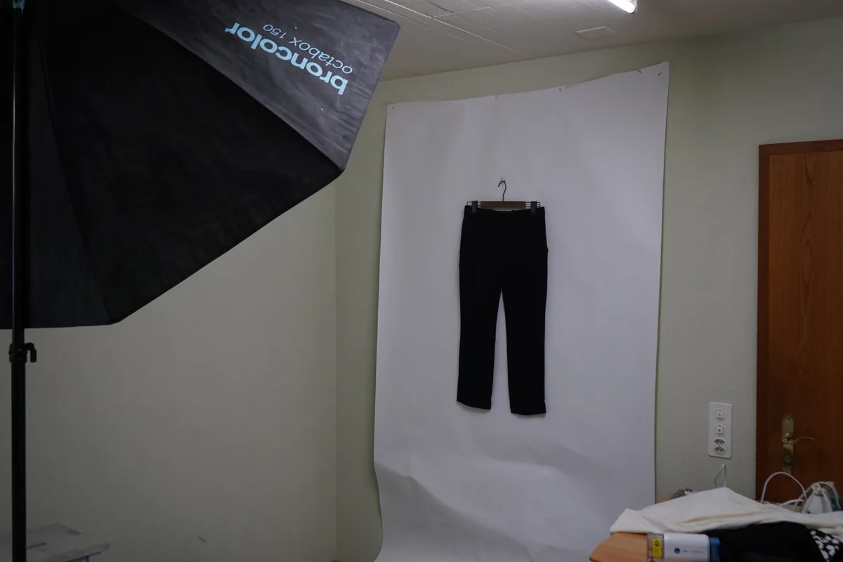 Eine schwarze Hose, welche vor einem weissen Hintergrund hängt.