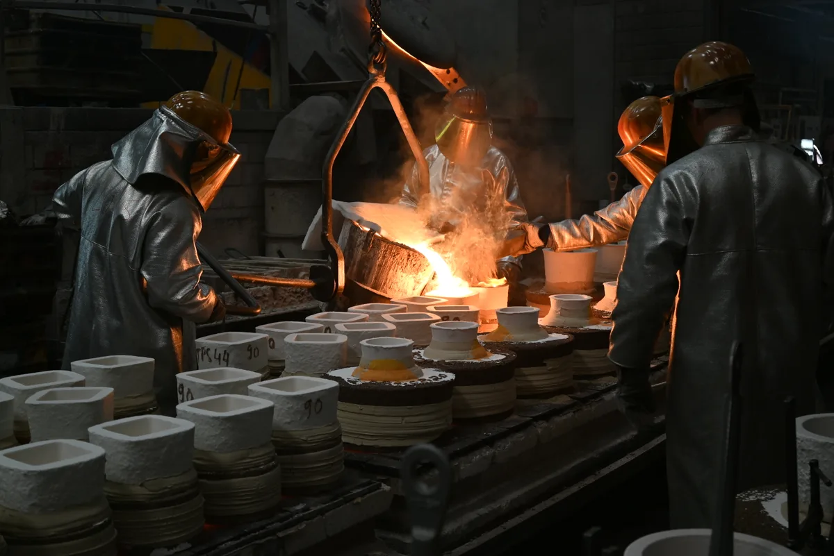 Arbeiter giessen flüssiges Metall in Gussformen.