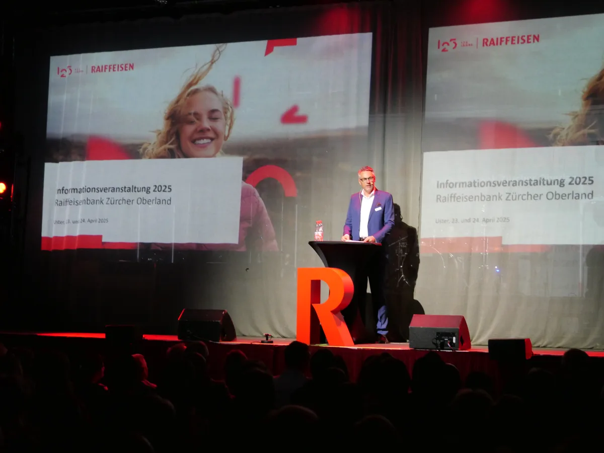Ein Mann steht auf einer Bühne und referiert. Vor dem Rednerpult steht ein grosses, rotes R.