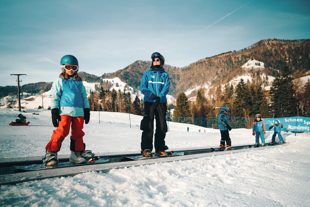 Kinder fahren mit Skiern und Snowboards auf einem Förderband.