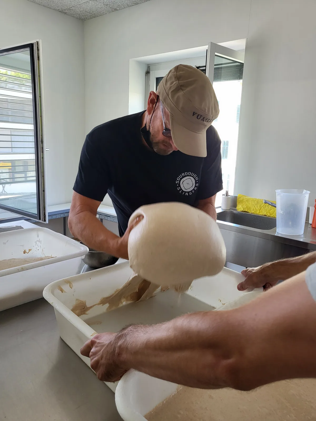 Ein Mann hebt einen grossen Sauerteig aus einem Plastikbottich.