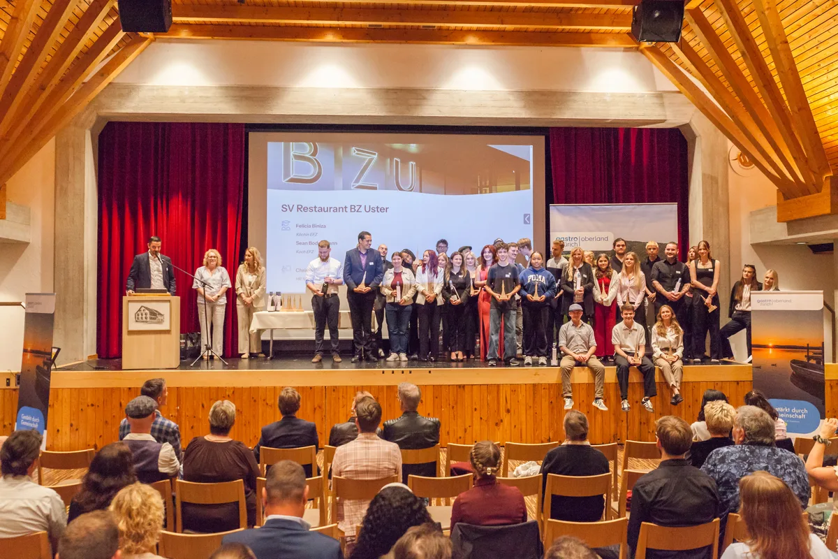 Ein würdiger Rahmen: Fabian Aegerter (links) zeichnete die erfolgreichen Lehrabgängerinnen und -abgänger von Gastro Zürich Oberland im Saal des Restaurants Rössli in Illnau aus. Gruppenbild mit vielen Lehrabgängern, die auf einer Bühne stehen.