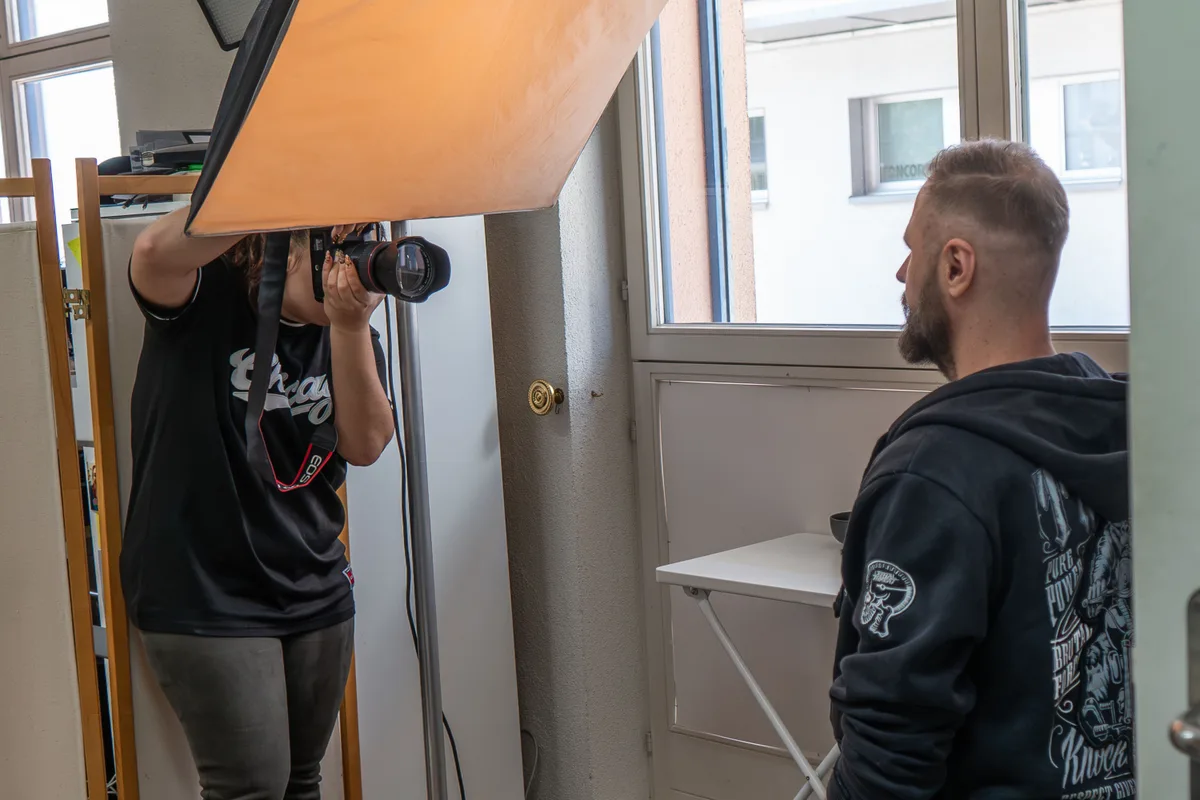 Eine Fotografin fotografiert in einem Studio einen bärtigen Mann.