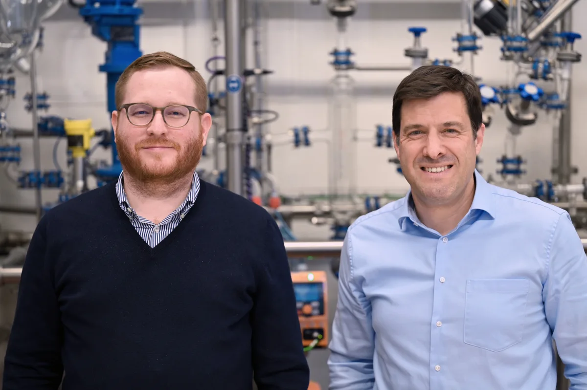 Eingespieltes Duo: CEO Silvio Büchi (links) und COO Jürg Krauer. Zwei Männer stehen vor einer Laboranlage mit Röhren und Glasbehälter.