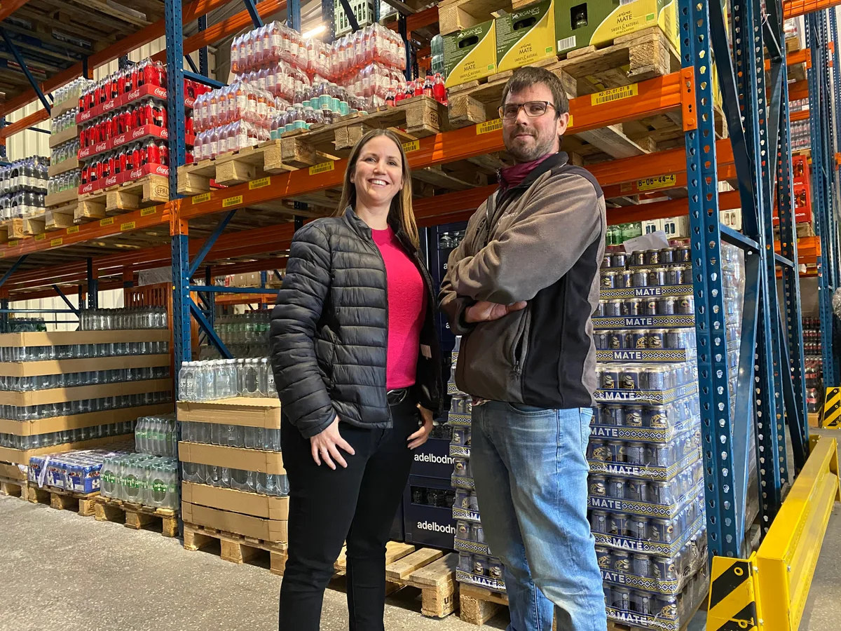 Daniela Brauchli Bucher leitet Verkauf und Marketing bei der Brauerei Uster, ihr Bruder Stefan Bucher ist für Produktion und Logistik verantwortlich. Daniela Brauchli Bucher und ihr Bruder Stefan Bucher stehen vor einem Hochregal mit Softdrinks. Sie trägt einen leuchtend roten Pullover unter einer dunklen Daunenjacke, er hat die Arme vor der Brust verschränkt.
