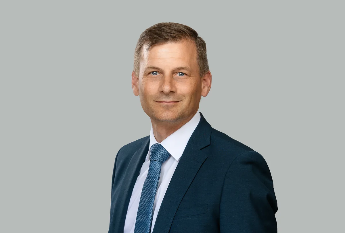 Porträt von Christoph Balmer. Er trägt einen dunkelblauen Anzug mit weissem Hemd und hellblauer Krawatte.