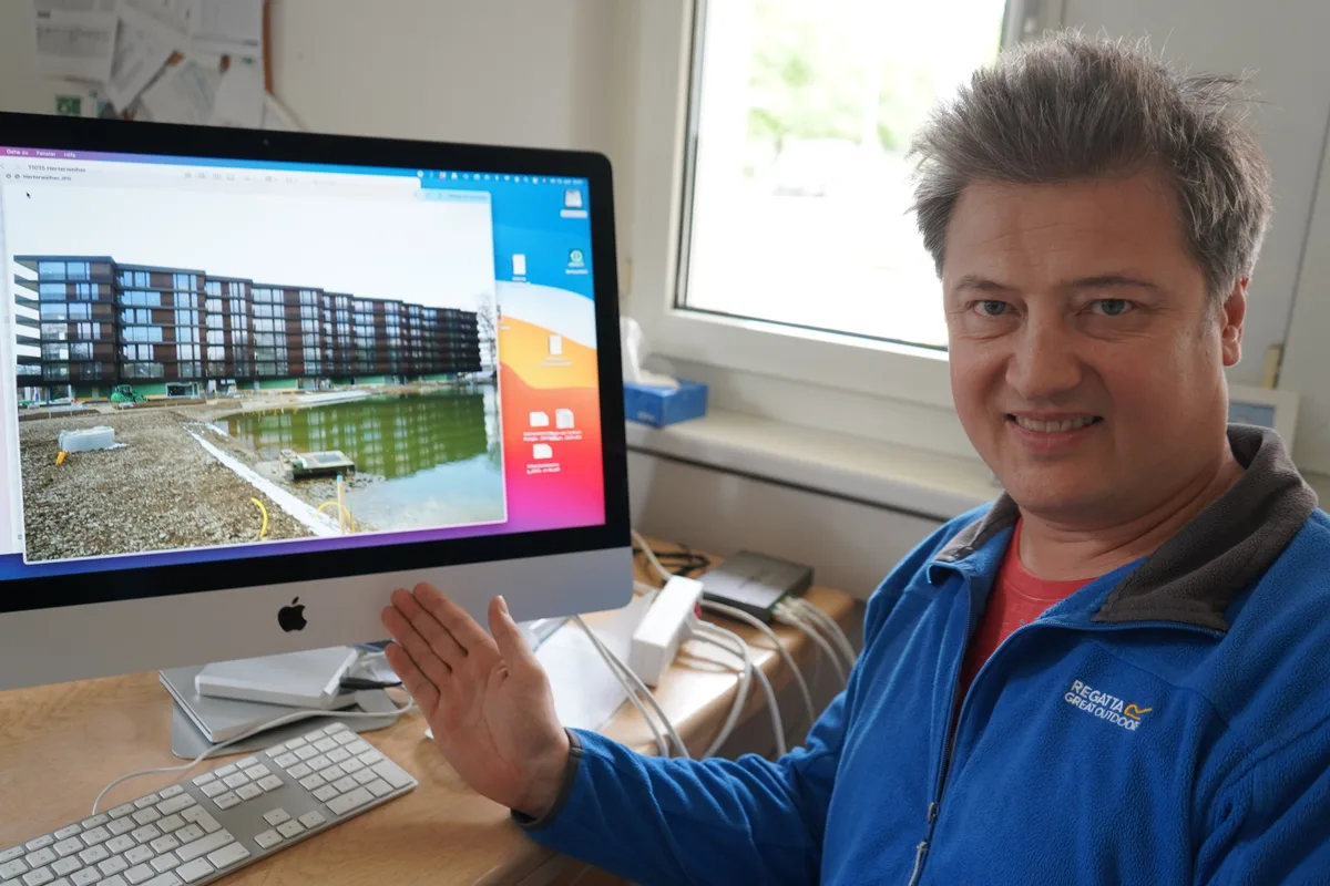 Ein Mann in einem blauen Pullover zeigt auf einen Bildschirm mit einem Wohnhaus.