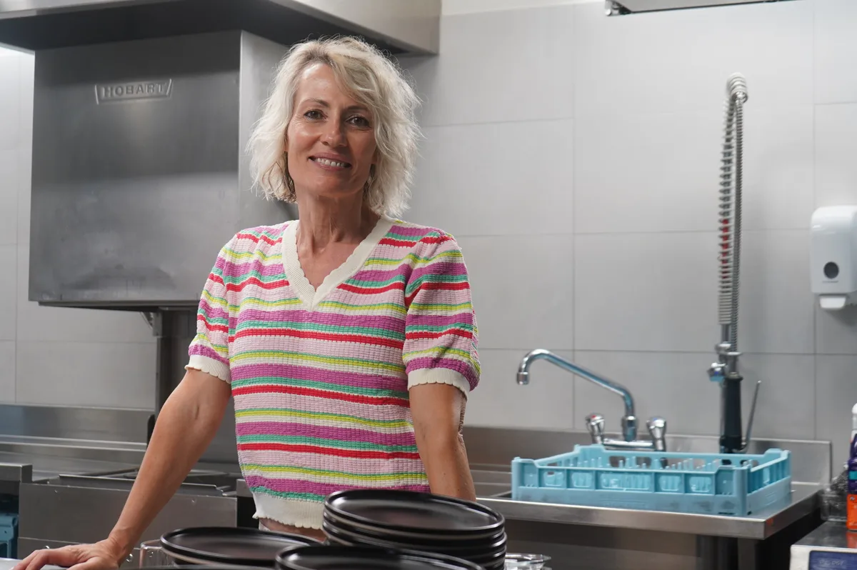 Eine Frau steht in einer Profi-Küche an einem Tisch und lächelt in die Kamera.