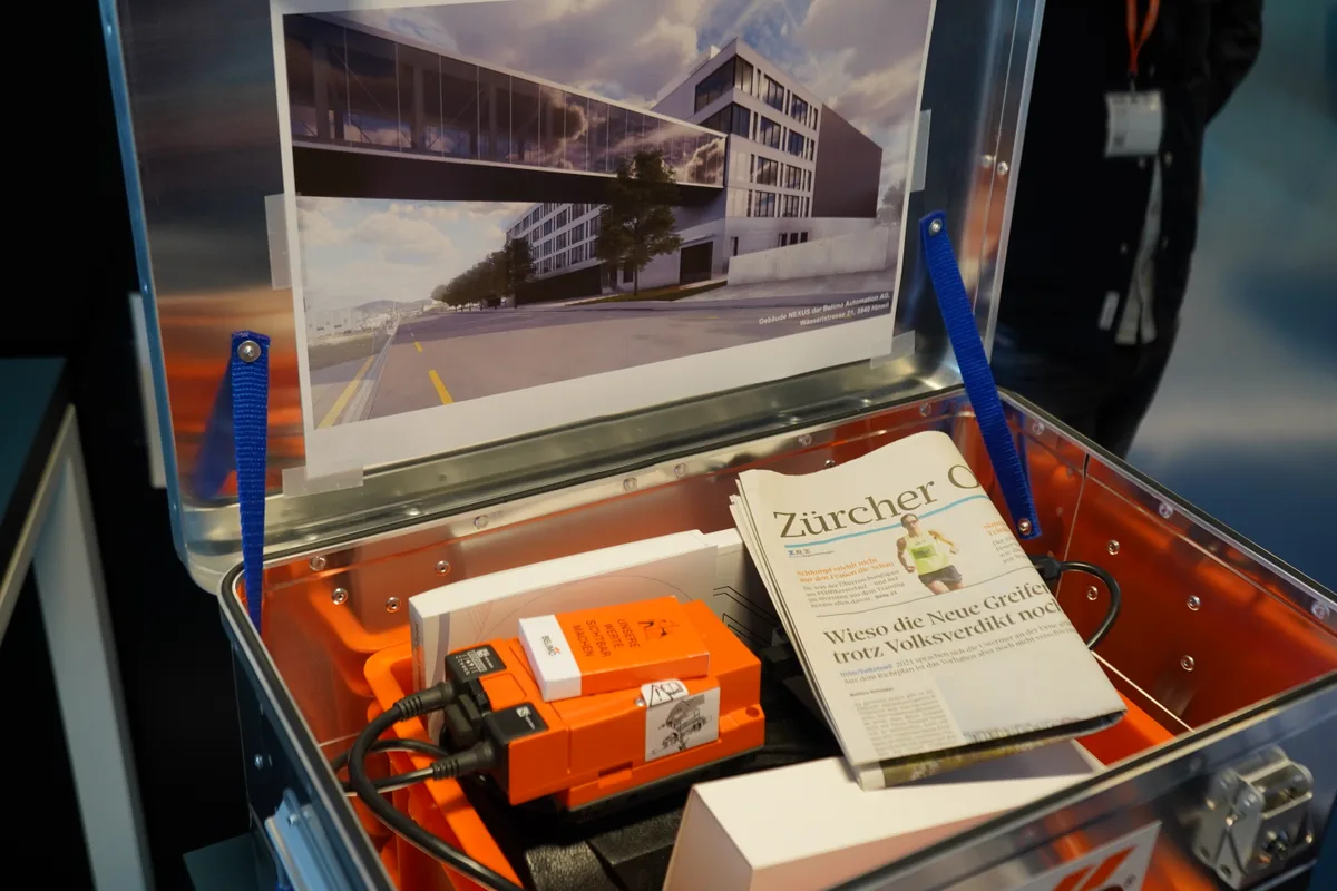 Eine Metalltruhe mit verschiedenen Produkten der Hinwiler Firma Belimo und einer Ausgabe des Zürcher Oberländers.