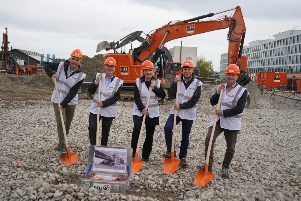 Vier Männer und eine Frau mit orangen Bauhelmen und orangen Schaufeln.