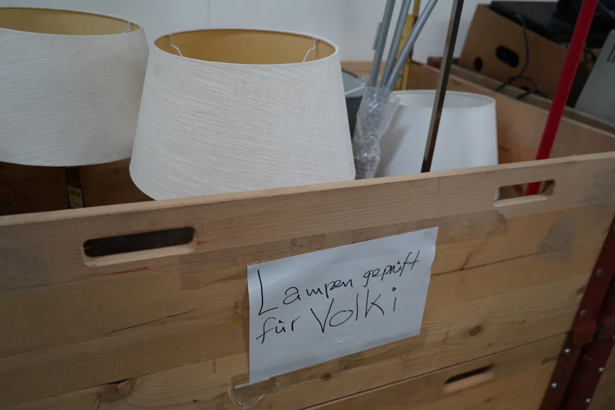 Ein Holzbehälter mit Lampen. Darauf klebt ein Zettel mit der Aufschrift "Lampen geprüft für Volki".