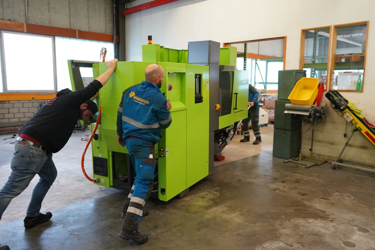 Männer schieben eine knallgrüne Maschine auf einem Handhubwagen.
