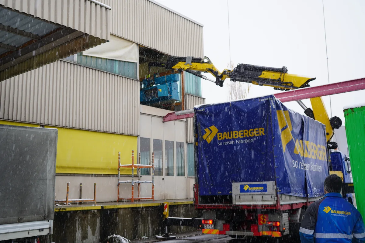 Ein Kran hievt eine Maschine aus dem zweiten Stock eines Industriegebäudes.